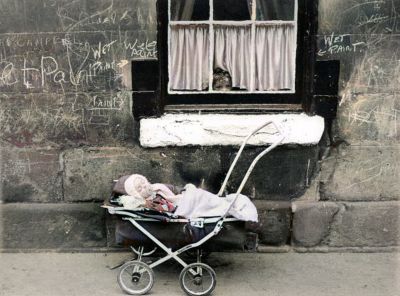 A Child looks at a Baby in a Pram from the Window of a Tenement Block
